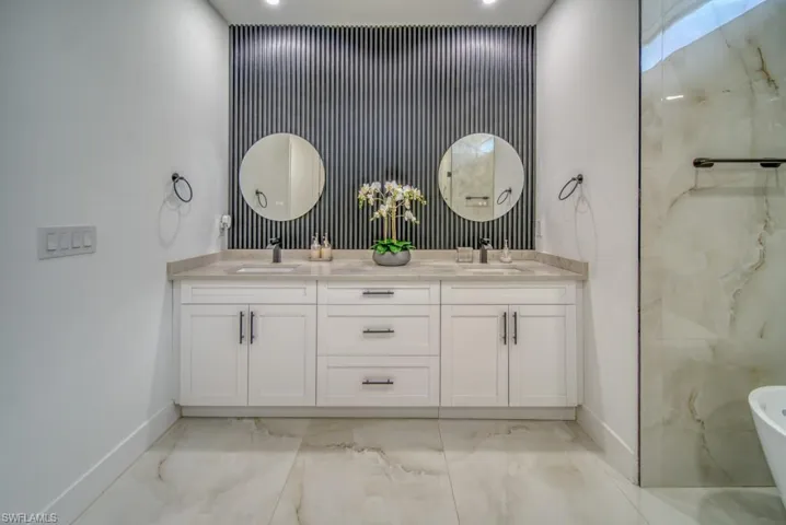 Full bath with light marble finish flooring, double vanity, and a soaking tub