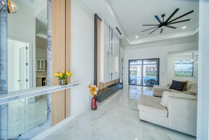 Living room featuring marble tiled floors, ceiling fan, a tray ceiling, a chandelier, and recessed lighting