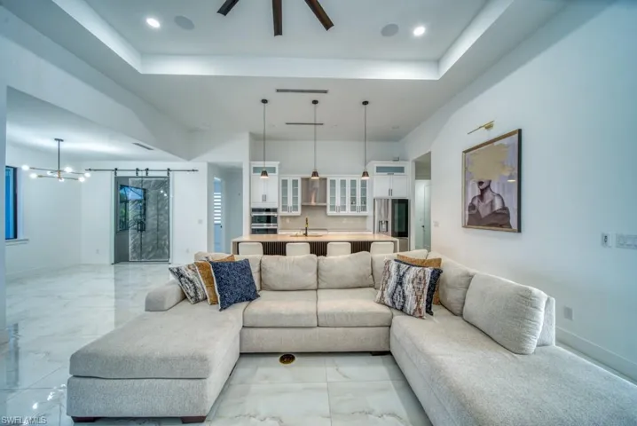 Living area with a barn door, a tray ceiling, a ceiling fan, and light marble finish floors