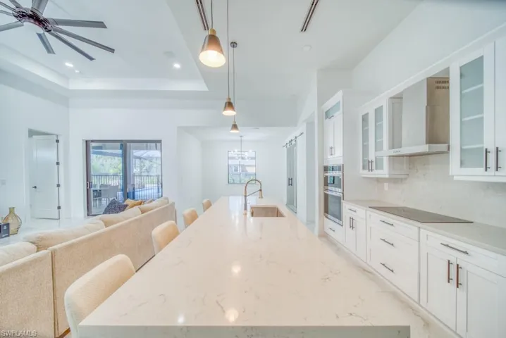 Kitchen featuring a kitchen bar, white cabinets, light stone counters, a large island, and decorative light fixtures
