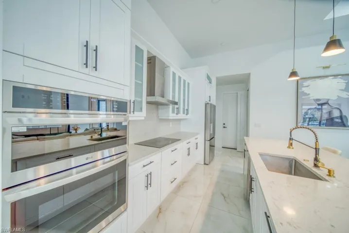 Kitchen featuring appliances with stainless steel finishes, light stone counters, light marble finish flooring, white cabinetry, and decorative light fixtures