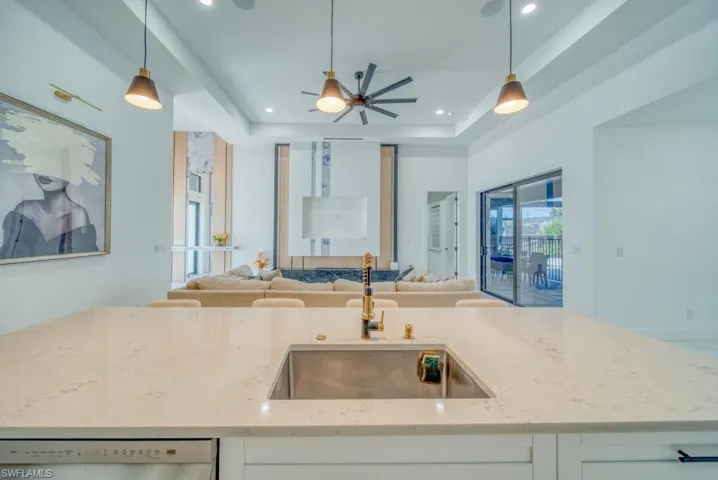 Kitchen featuring a raised ceiling, a center island with sink, light stone countertops, pendant lighting, and open floor plan