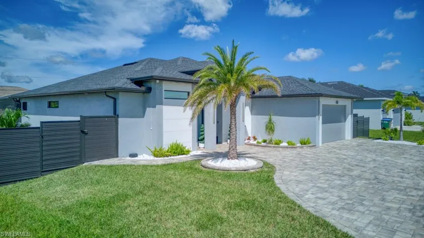 Back of house featuring stucco siding, decorative driveway, an attached garage, a shingled roof, and a gate