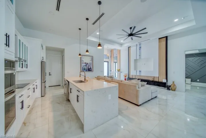 Kitchen with white cabinets, light marble finish flooring, pendant lighting, light stone counters, and open floor plan