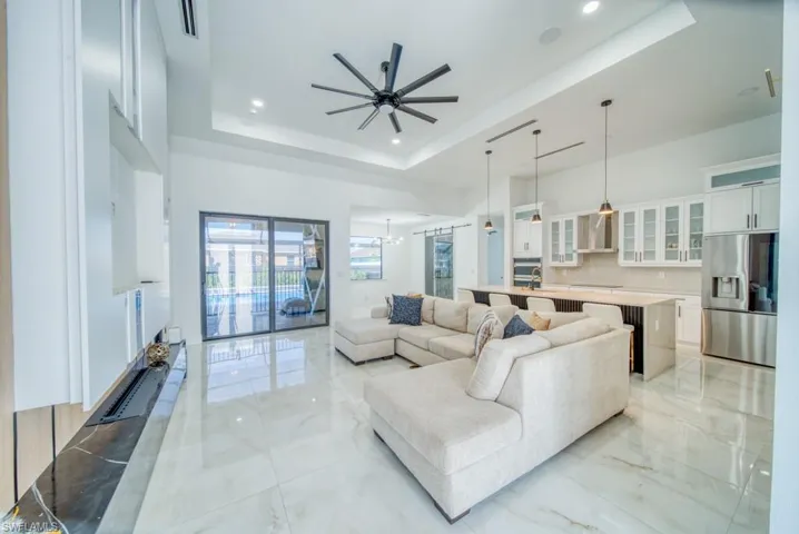 Living room featuring a raised ceiling, light marble finish flooring, recessed lighting, a chandelier, and ceiling fan
