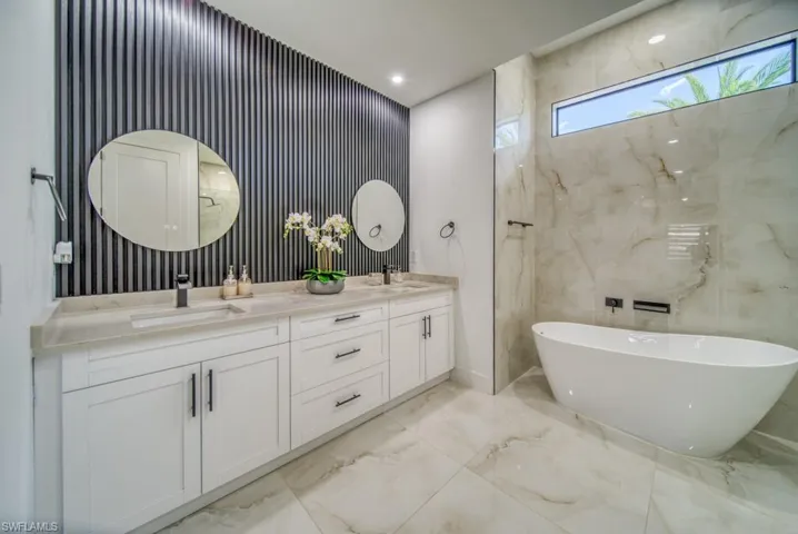 Full bathroom featuring light marble finish floors, a freestanding bath, double vanity, recessed lighting, and wallpapered walls