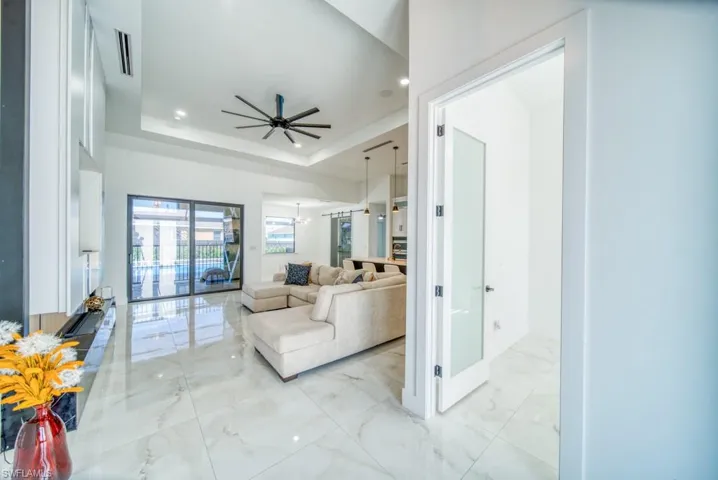 Living area featuring light marble finish flooring, a ceiling fan, a raised ceiling, recessed lighting, and a chandelier