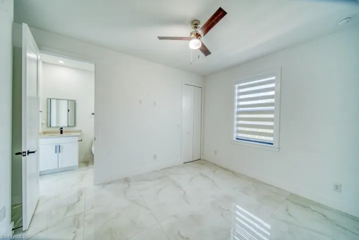 Unfurnished bedroom featuring a ceiling fan, light marble finish floors, ensuite bath, and a closet