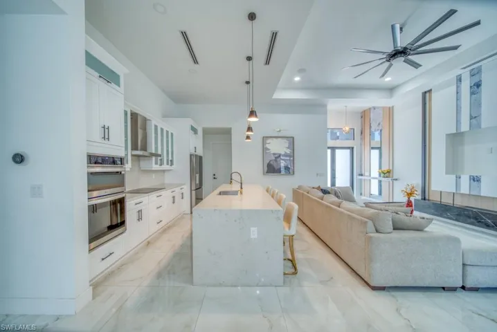 Kitchen with a kitchen breakfast bar, white cabinets, hanging light fixtures, light marble finish floors, and light stone counters