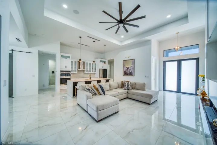Living area with a barn door, a tray ceiling, light marble finish floors, a towering ceiling, and recessed lighting
