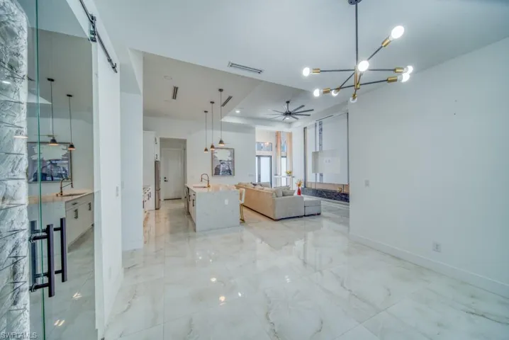 Living room featuring a chandelier, a ceiling fan, light marble finish floors, a raised ceiling, and a barn door