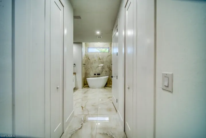Bathroom featuring light marble finish flooring, a freestanding bath, and vanity