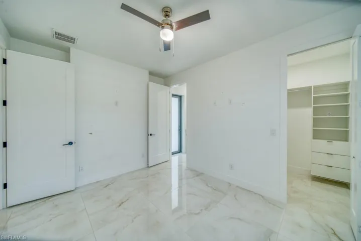 Unfurnished bedroom featuring marble finish flooring, a walk in closet, and ceiling fan