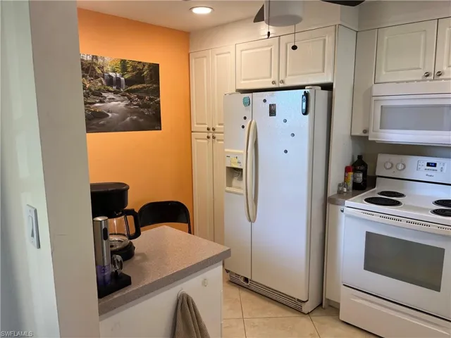 Kitchen featuring white appliances, white cabinetry, light tile patterned floors, and recessed lighting
