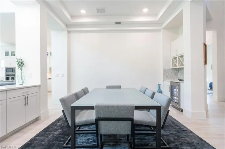 Dining room with visible vents, a raised ceiling, beverage cooler, a bar, and light wood-style floors