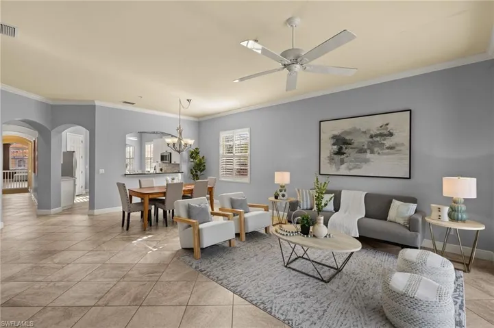Living area featuring arched walkways, crown molding, and ceiling fan with notable chandelier