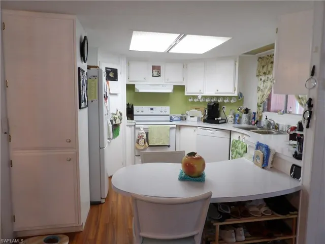 Kitchen with white appliances, a peninsula, white cabinets, and light countertops