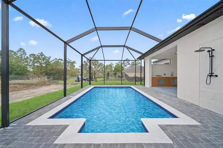 Outdoor pool with a sunroom, a patio area, glass enclosure, and a yard