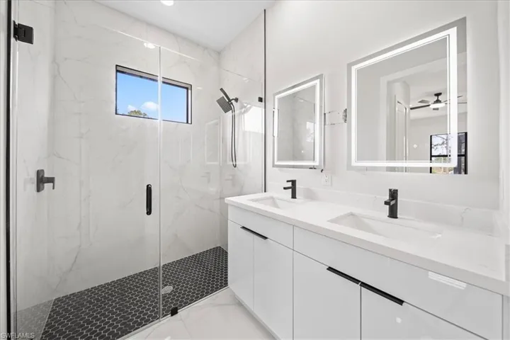 Bathroom featuring double vanity, a marble finish shower, light marble finish flooring, and a ceiling fan