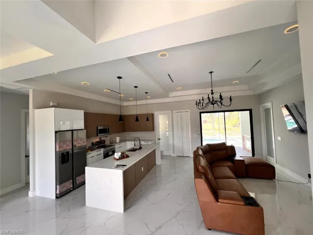 Open-concept living space featuring a gourmet kitchen, large center island with integrated sink, recessed lighting, and tray ceilings