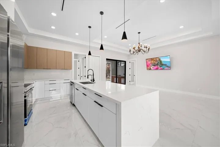 Dual tone kitchen featuring modern cabinets, stainless steel appliances, a tray ceiling, light marble finish floors, and two tone cabinetry