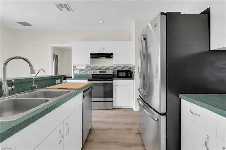Kitchen with appliances with stainless steel finishes, white cabinetry, backsplash, light wood-style floors, and recessed lighting
