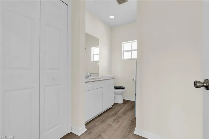 Half bathroom featuring a closet, vanity, light wood-type flooring, and recessed lighting