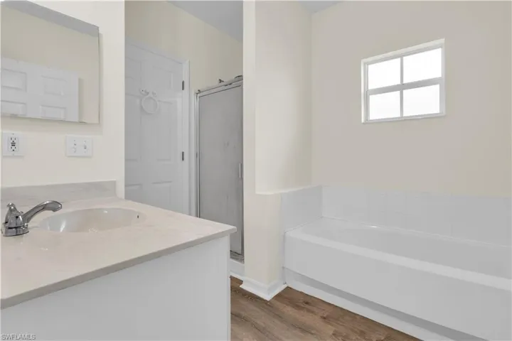 Full bath featuring vanity, a garden tub, a shower stall, and wood finished floors