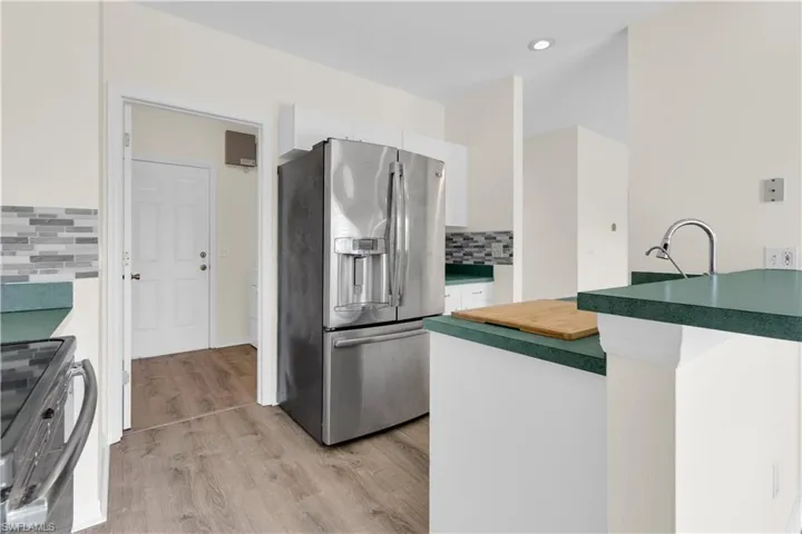Kitchen featuring stainless steel appliances, light wood-type flooring, decorative backsplash, white cabinets, and butcher block countertops