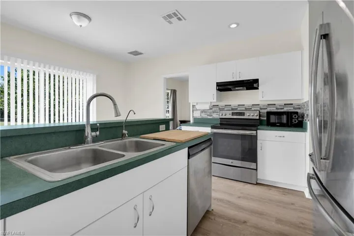 Kitchen featuring appliances with stainless steel finishes, white cabinetry, decorative backsplash, recessed lighting, and under cabinet range hood