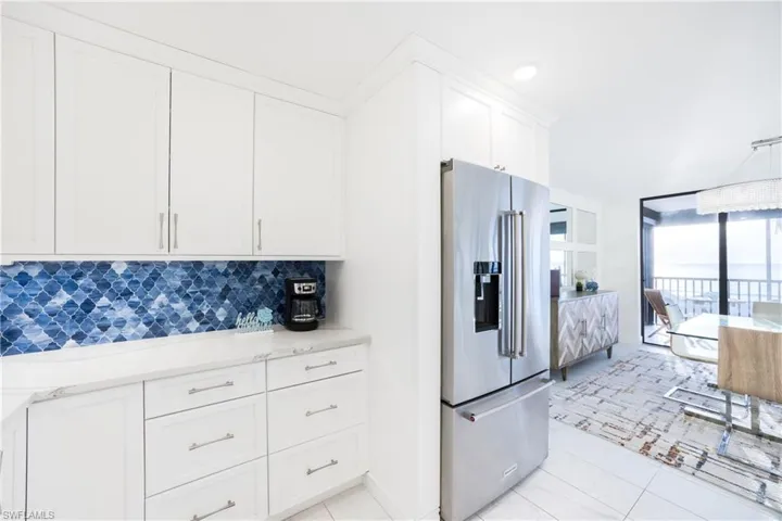 Kitchen featuring high quality fridge, white cabinetry, backsplash, a wall of windows, and light stone countertops