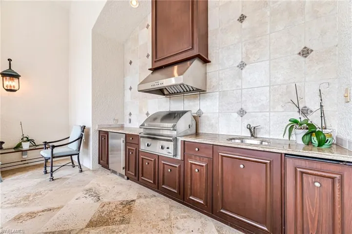 Kitchen with light stone countertops, sink, tasteful backsplash, stainless steel fridge, and exhaust hood