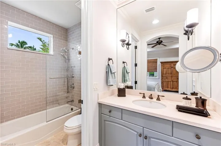 Full bathroom with vanity, ceiling fan, tiled shower / bath combo, toilet, and ornamental molding