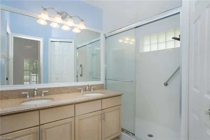 Bathroom with a shower with door, large vanity, and double sink