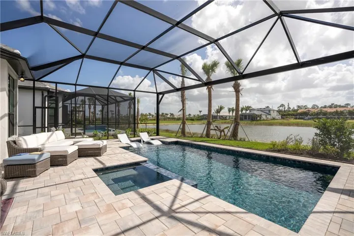 View of swimming pool with glass enclosure, a water view, a sunroom, a pool with connected hot tub, and a patio