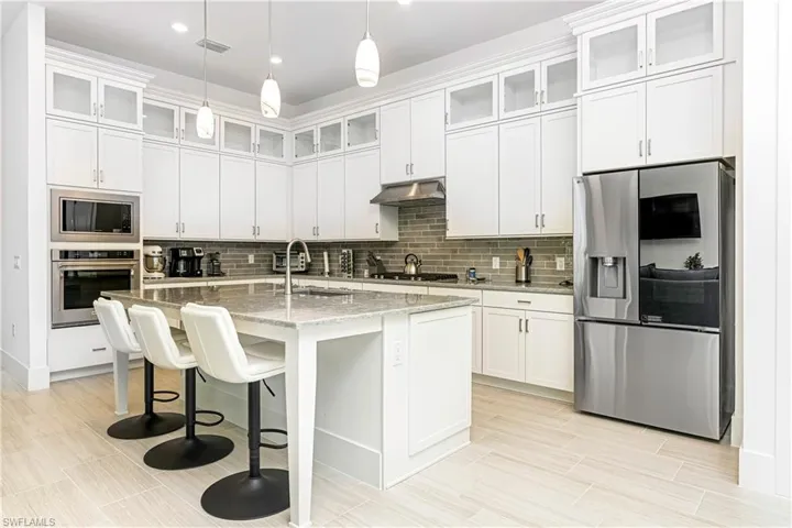 Kitchen with stainless steel appliances, a breakfast bar area, white cabinetry, light stone counters, and recessed lighting