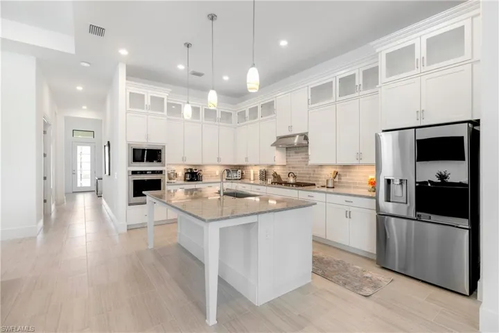 Kitchen featuring glass insert cabinets, appliances with stainless steel finishes, light stone countertops, white cabinets, and recessed lighting