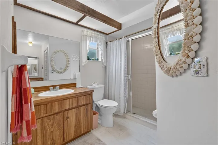 Wood-finish vanity with an integrated sink, large wall-mounted mirror, and a shower enclosure