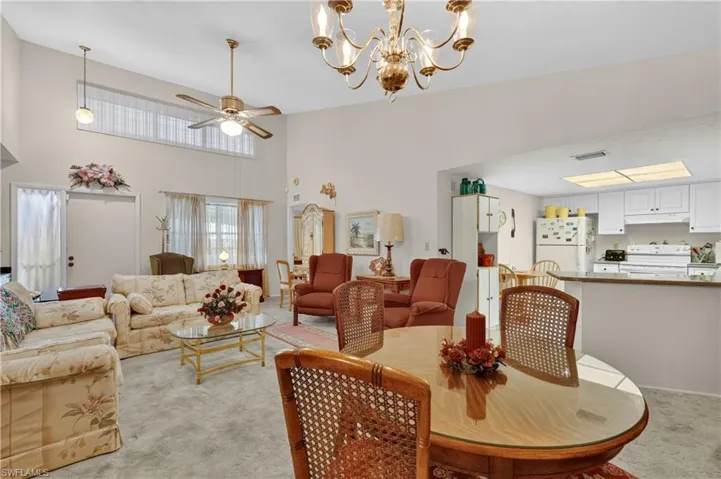 Vaulted ceiling with transom window, ceiling fan, and chandelier
