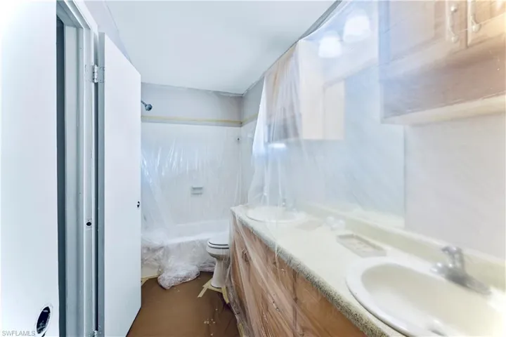 Full bathroom featuring tiled shower / bath combo, toilet, and double vanity