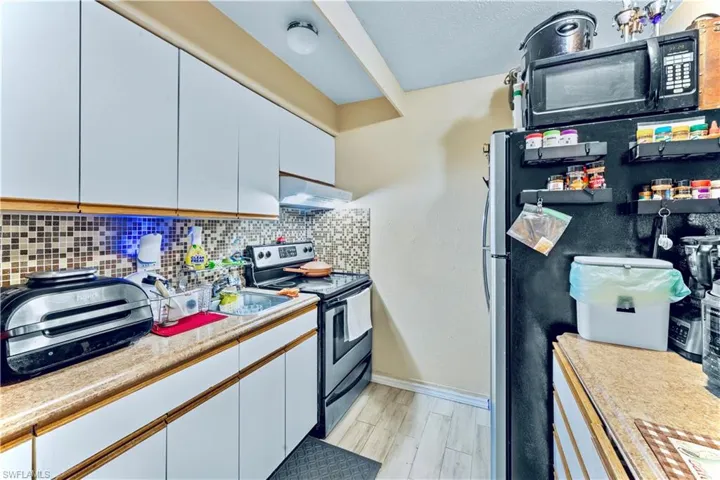 Kitchen with white cabinetry, light hardwood / wood-style floors, wall chimney exhaust hood, and electric stove