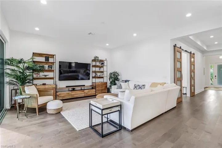 Living area featuring a barn door, recessed lighting, light wood-style floors, and a raised ceiling