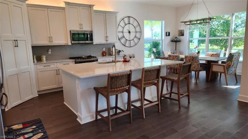 Kitchen with appliances with stainless steel finishes, light stone countertops, an island with sink, backsplash, and a kitchen breakfast bar