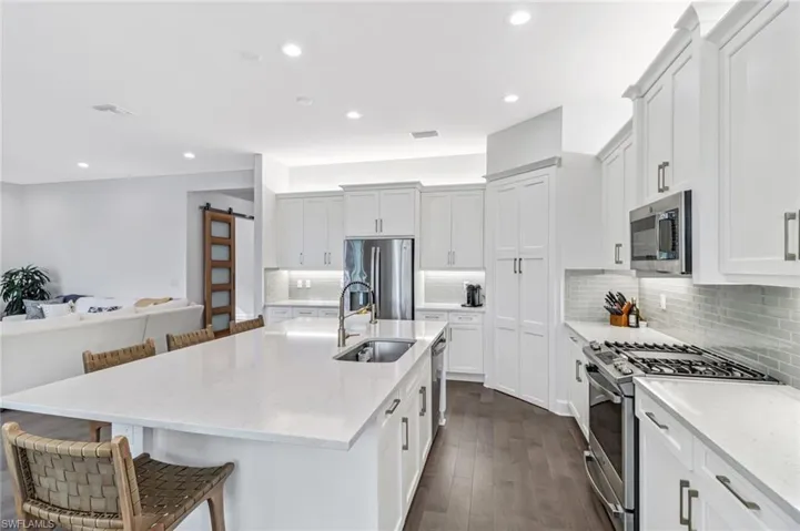Kitchen with stainless steel appliances, a barn door, a breakfast bar, light stone countertops, and decorative backsplash
