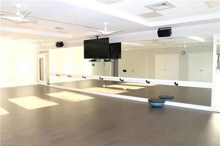 Exercise room with ceiling fan, wood finished floors, a raised ceiling, and visible vents