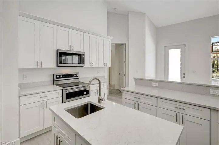 Kitchen with appliances with stainless steel finishes, a sink, light wood-type flooring, white cabinets, and light stone countertops