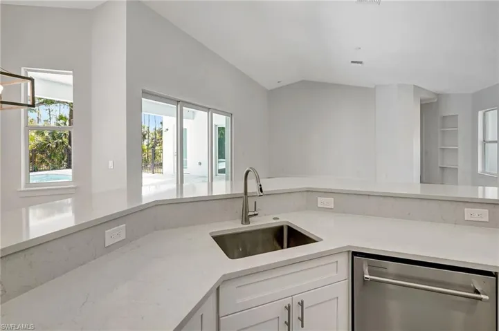 Kitchen with dishwasher, a sink, white cabinets, healthy amount of natural light, and vaulted ceiling