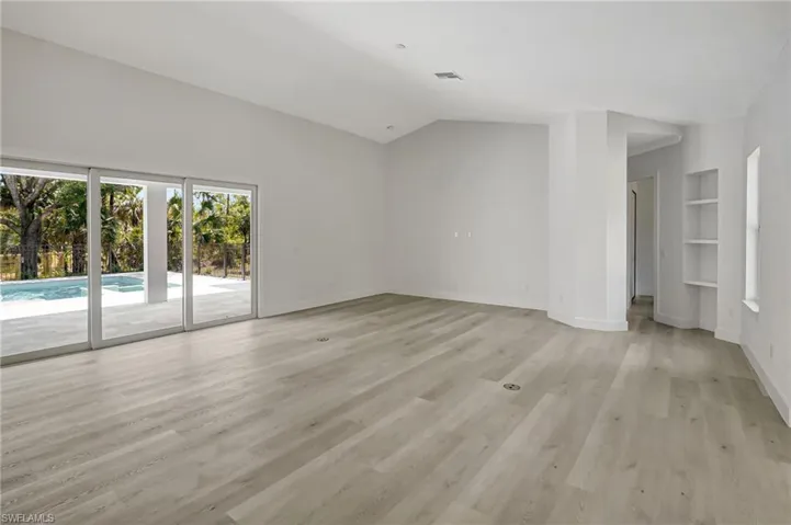 Unfurnished living room featuring light wood finished floors, baseboards, built in features, and vaulted ceiling