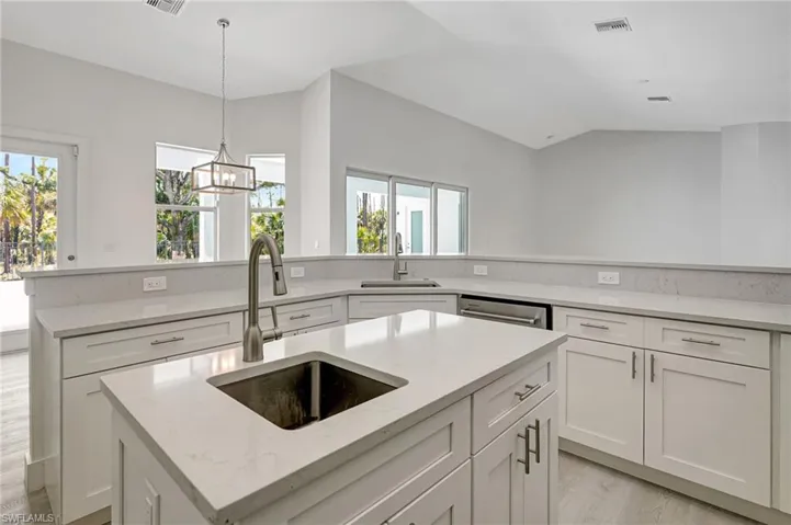 Kitchen with a sink, an island with sink, white cabinets, and vaulted ceiling