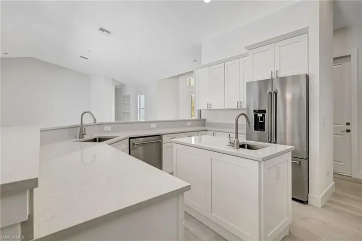 Kitchen featuring stainless steel appliances, a center island with sink, a sink, light wood-style floors, and vaulted ceiling
